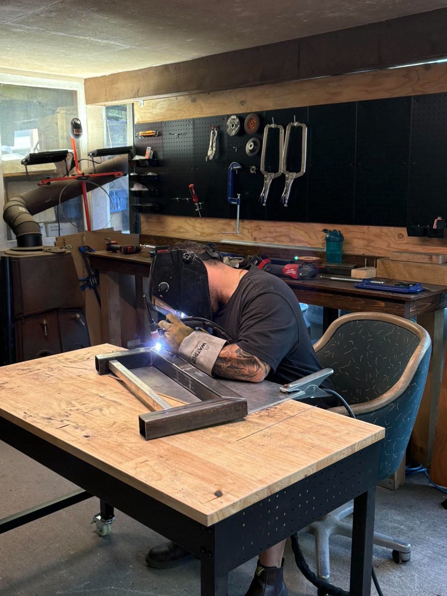 Welder TIG welding a square steel tube frame section at a workbench
